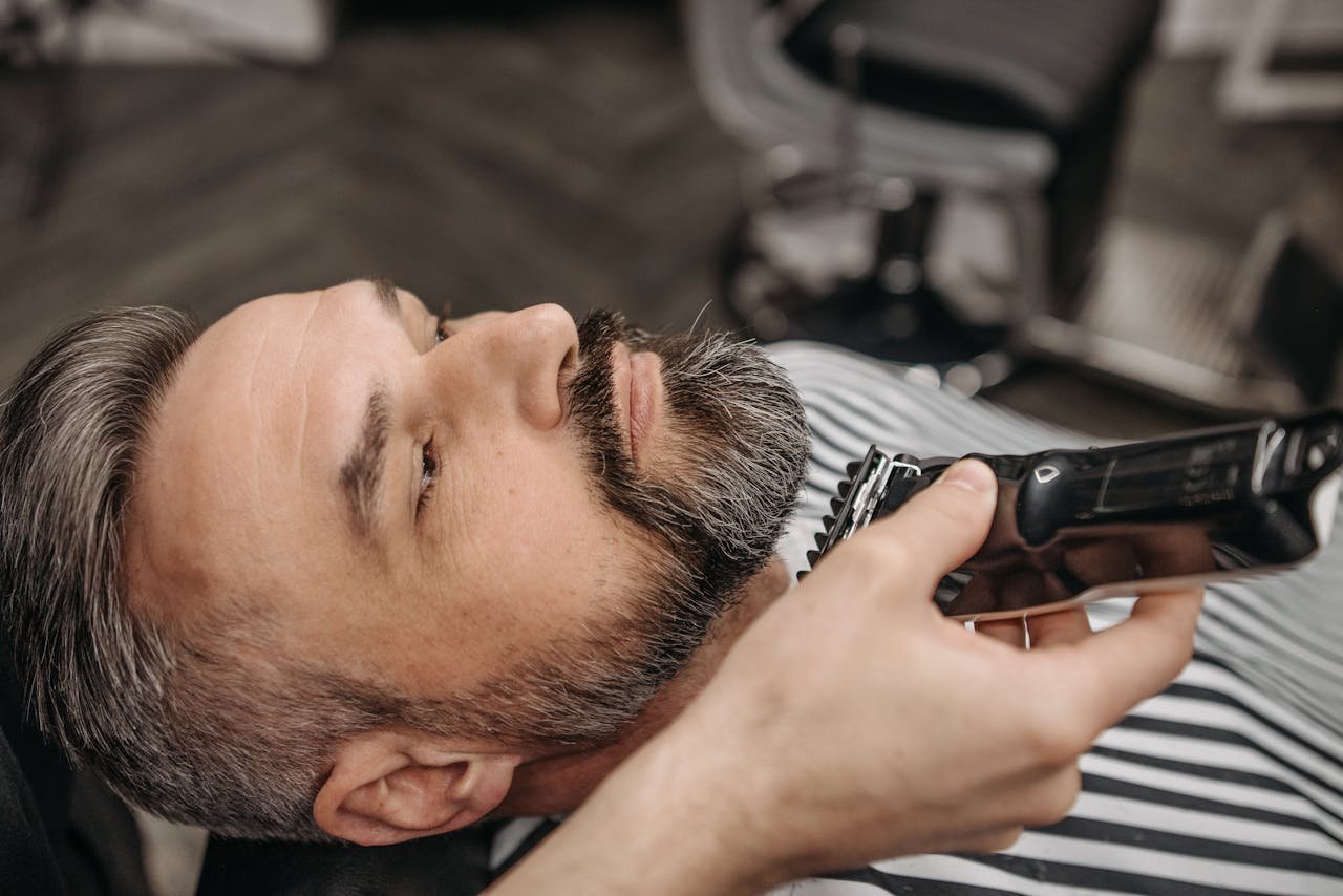 Close-up of a man getting a beard trim at a barbershop with a hair clipper.